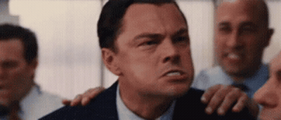 A Man In A Suit And Tie Is Standing In Front Of A Group Of Men And Making A Funny Face . GIF