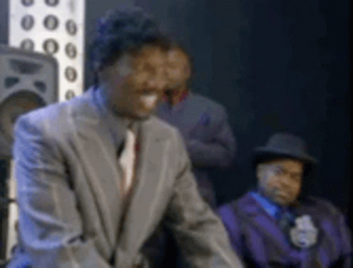 A Man In A Suit And Tie Is Standing In Front Of A Group Of Men . GIF