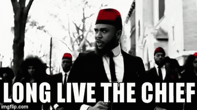 A Man In A Suit And Tie Is Standing In Front Of A Group Of Men Wearing Red Hats And Ties . GIF