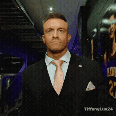 A Man In A Suit And Tie Is Standing In Front Of A Hawks Jersey GIF