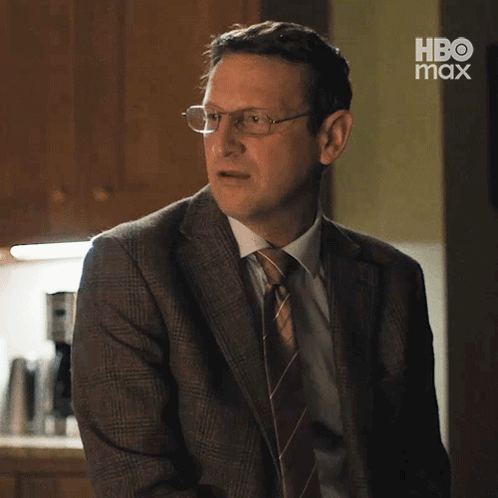 A Man In A Suit And Tie Is Standing In Front Of A Hbo Max Sign . GIF