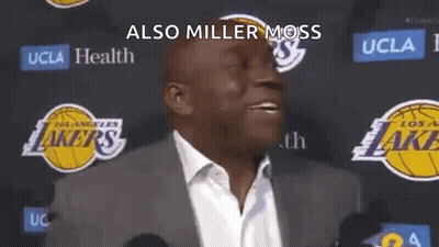 A Man In A Suit And Tie Is Standing In Front Of A Lakers Logo And Talking To The Media . GIF