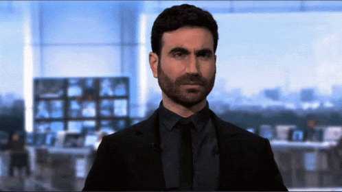 A Man In A Suit And Tie Is Standing In Front Of A Large Window GIF