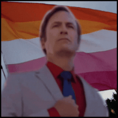 A Man In A Suit And Tie Is Standing In Front Of A Lesbian Flag GIF