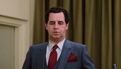 A Man In A Suit And Tie Is Standing In Front Of A Microphone And Making A Funny Face . GIF