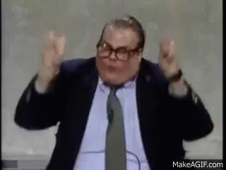 A Man In A Suit And Tie Is Standing In Front Of A Microphone And Making A Funny Face . GIF