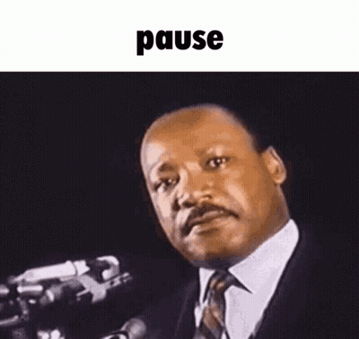 A Man In A Suit And Tie Is Standing In Front Of A Microphone And Making A Funny Face . GIF