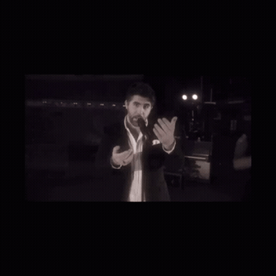 A Man In A Suit And Tie Is Standing In Front Of A Microphone GIF
