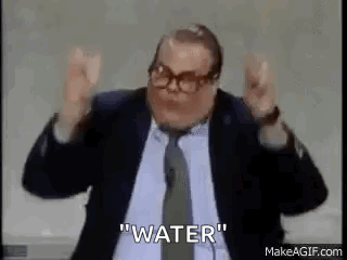 A Man In A Suit And Tie Is Standing In Front Of A Microphone With His Hands In The Air . GIF