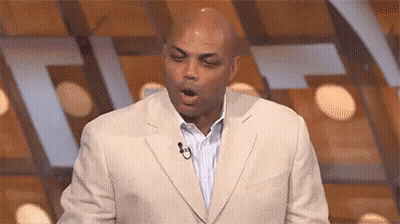 A Man In A Suit And Tie Is Standing In Front Of A Microphone With His Mouth Open . GIF