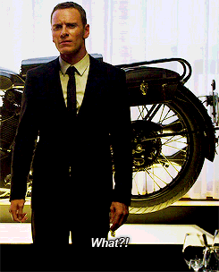 A Man In A Suit And Tie Is Standing In Front Of A Motorcycle And Says What GIF
