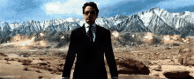 A Man In A Suit And Tie Is Standing In Front Of A Mountain Range GIF