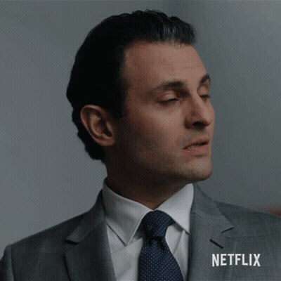 A Man In A Suit And Tie Is Standing In Front Of A Netflix Sign GIF