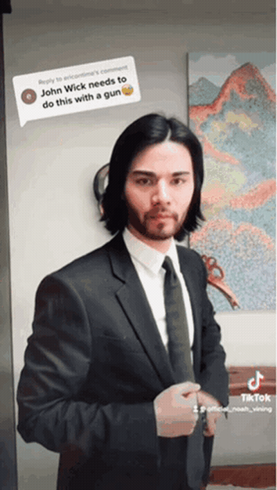 A Man In A Suit And Tie Is Standing In Front Of A Painting That Says John Wick GIF