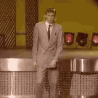 A Man In A Suit And Tie Is Standing In Front Of A Piano On A Stage . GIF
