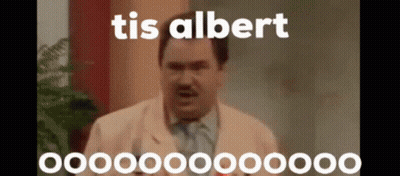 A Man In A Suit And Tie Is Standing In Front Of A Plant And Talking . GIF