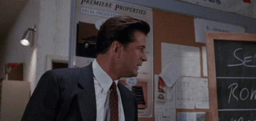 A Man In A Suit And Tie Is Standing In Front Of A Premiere Properties Sign GIF