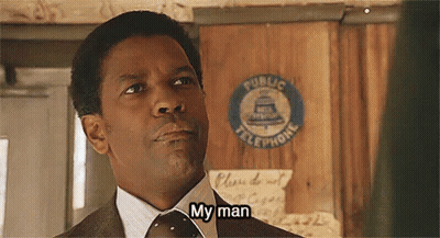 A Man In A Suit And Tie Is Standing In Front Of A Public Telephone Sign And Saying `` My Man '' . GIF