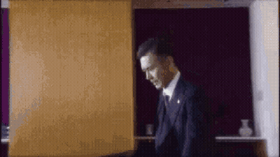 A Man In A Suit And Tie Is Standing In Front Of A Purple Wall In A Room . GIF