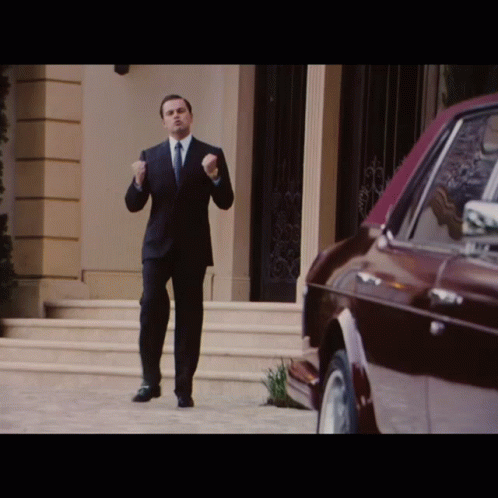 A Man In A Suit And Tie Is Standing In Front Of A Red Car GIF