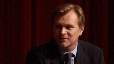 A Man In A Suit And Tie Is Standing In Front Of A Red Curtain And Smiling . GIF