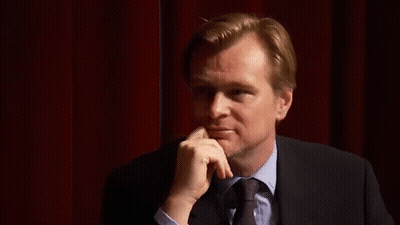 A Man In A Suit And Tie Is Standing In Front Of A Red Curtain . GIF