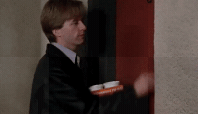A Man In A Suit And Tie Is Standing In Front Of A Red Door Holding A Tray Of Pills . GIF