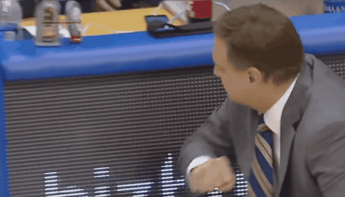 A Man In A Suit And Tie Is Standing In Front Of A Scoreboard That Says ' Denver ' On It GIF