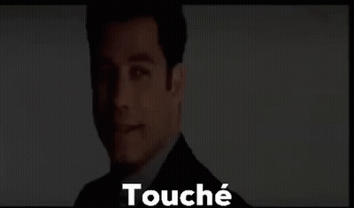A Man In A Suit And Tie Is Standing In Front Of A Screen With The Words Touché Written On It . GIF