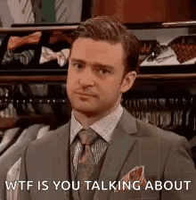A Man In A Suit And Tie Is Standing In Front Of A Shelf Of Ties . GIF