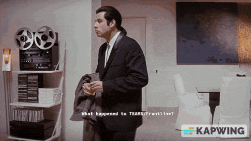 A Man In A Suit And Tie Is Standing In Front Of A Shelf That Says What Happened To Teams/frontline GIF