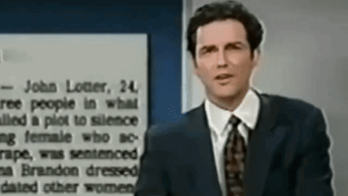A Man In A Suit And Tie Is Standing In Front Of A Sign That Says John Loiter GIF