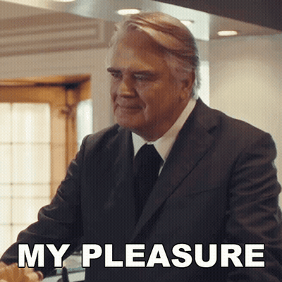 A Man In A Suit And Tie Is Standing In Front Of A Sign That Says " My Pleasure " GIF