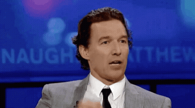 A Man In A Suit And Tie Is Standing In Front Of A Sign That Says Naughey Matthew GIF