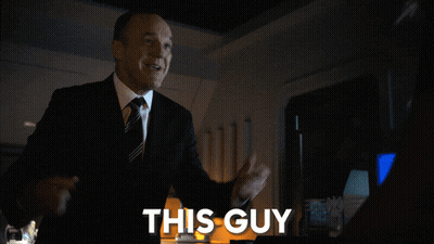 A Man In A Suit And Tie Is Standing In Front Of A Sign That Says This Guy GIF