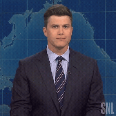 A Man In A Suit And Tie Is Standing In Front Of A Snl Sign GIF