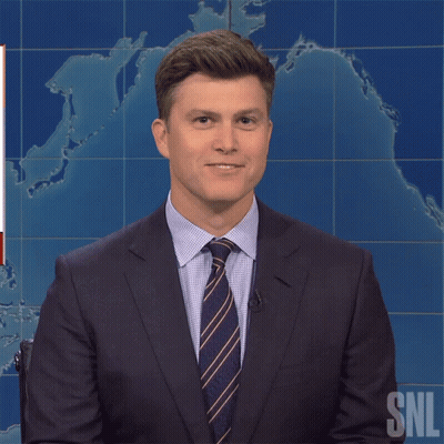 A Man In A Suit And Tie Is Standing In Front Of A Snl Sign GIF