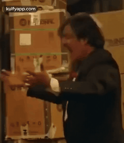 A Man In A Suit And Tie Is Standing In Front Of A Stack Of Boxes . GIF