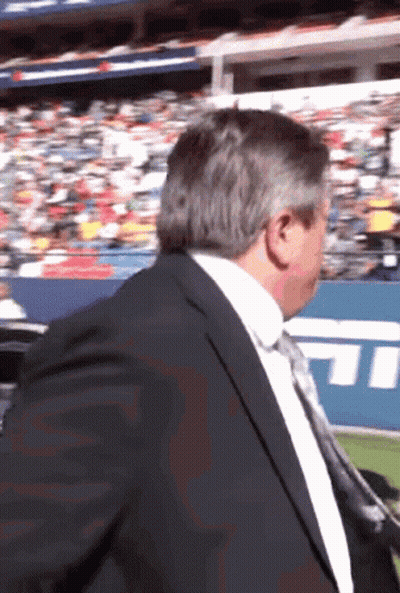 A Man In A Suit And Tie Is Standing In Front Of A Stadium With The Letters Tnt On It GIF