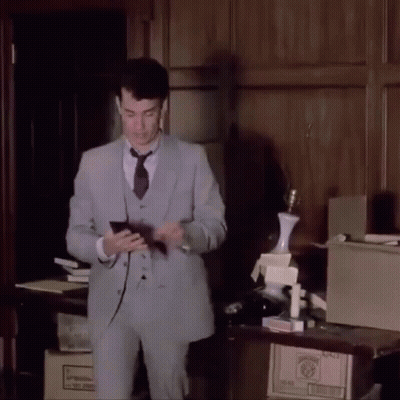 A Man In A Suit And Tie Is Standing In Front Of A Table With Boxes On It And A Lamp On Top GIF