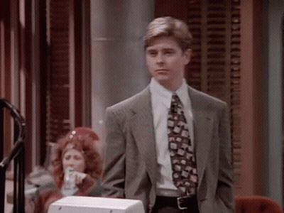 A Man In A Suit And Tie Is Standing In Front Of A Telephone GIF