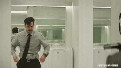 A Man In A Suit And Tie Is Standing In Front Of A Urinal In A Mission Impossible Scene GIF