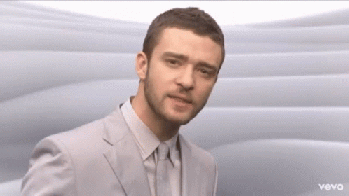 A Man In A Suit And Tie Is Standing In Front Of A Vevo Logo GIF