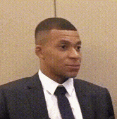 A Man In A Suit And Tie Is Standing In Front Of A Wall And Looking At The Camera . GIF