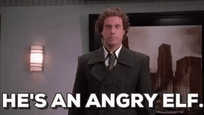 A Man In A Suit And Tie Is Standing In Front Of A Wall And Says `` He 'S An Angry Elf '' . GIF