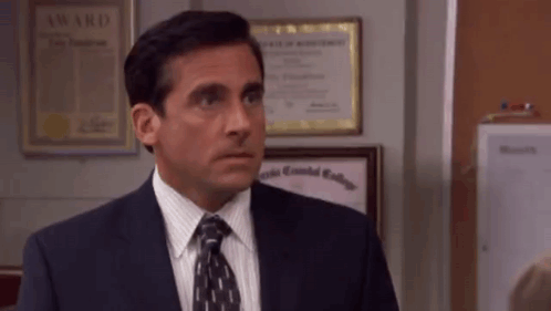 A Man In A Suit And Tie Is Standing In Front Of A Wall . GIF