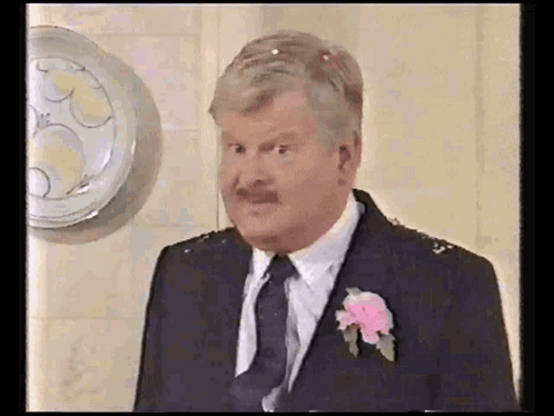 A Man In A Suit And Tie Is Standing In Front Of A Wall . GIF