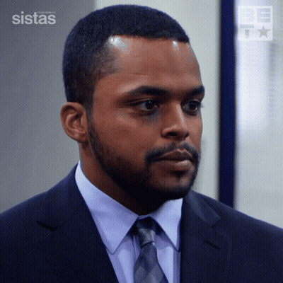 A Man In A Suit And Tie Is Standing In Front Of A Wall That Says Sistas GIF
