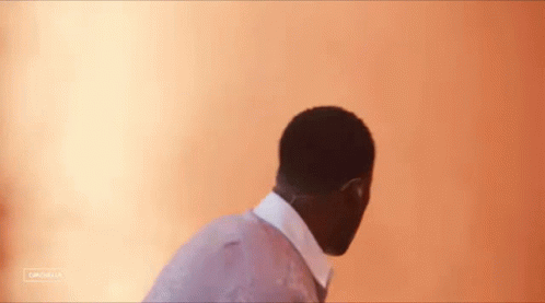 A Man In A Suit And Tie Is Standing In Front Of A Wall With A Blurred Background . GIF