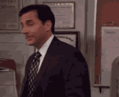 A Man In A Suit And Tie Is Standing In Front Of A Wall With Awards On It . GIF